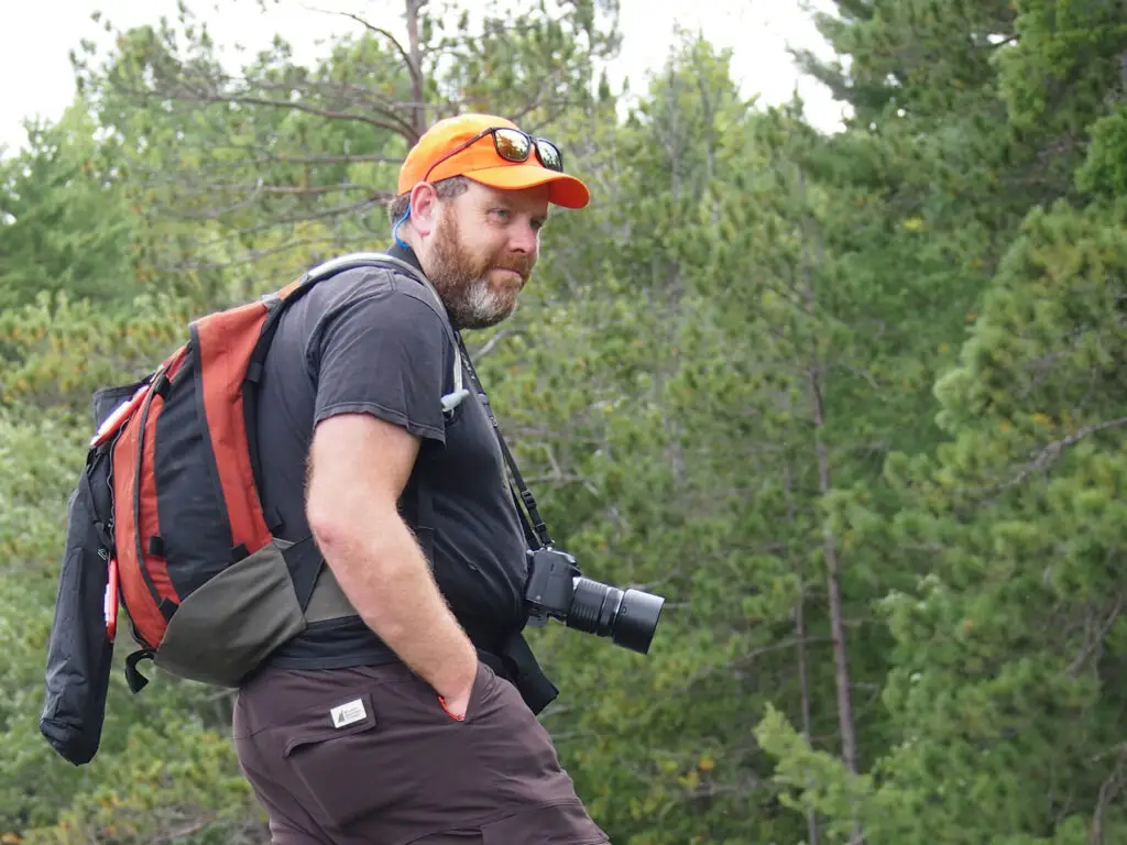 Jeff smiles with his camera and backpack on
